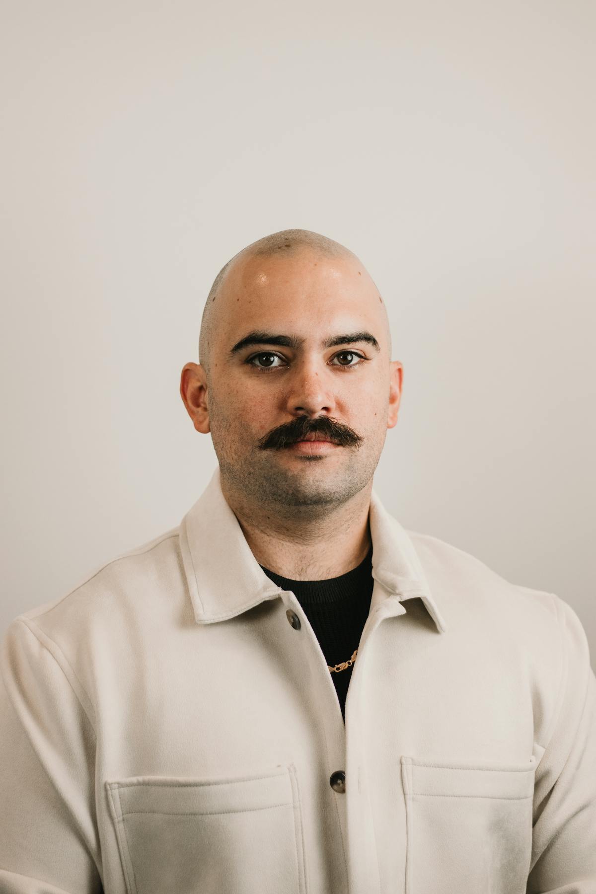 Studio portrait of a bald man with a dark mustache in a cream jacket
