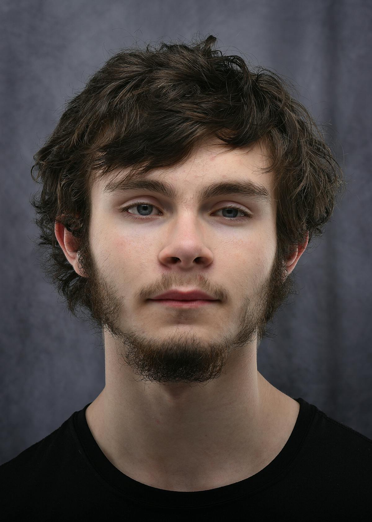 Senior portrait of a young man with wavy hair against a gray backdrop