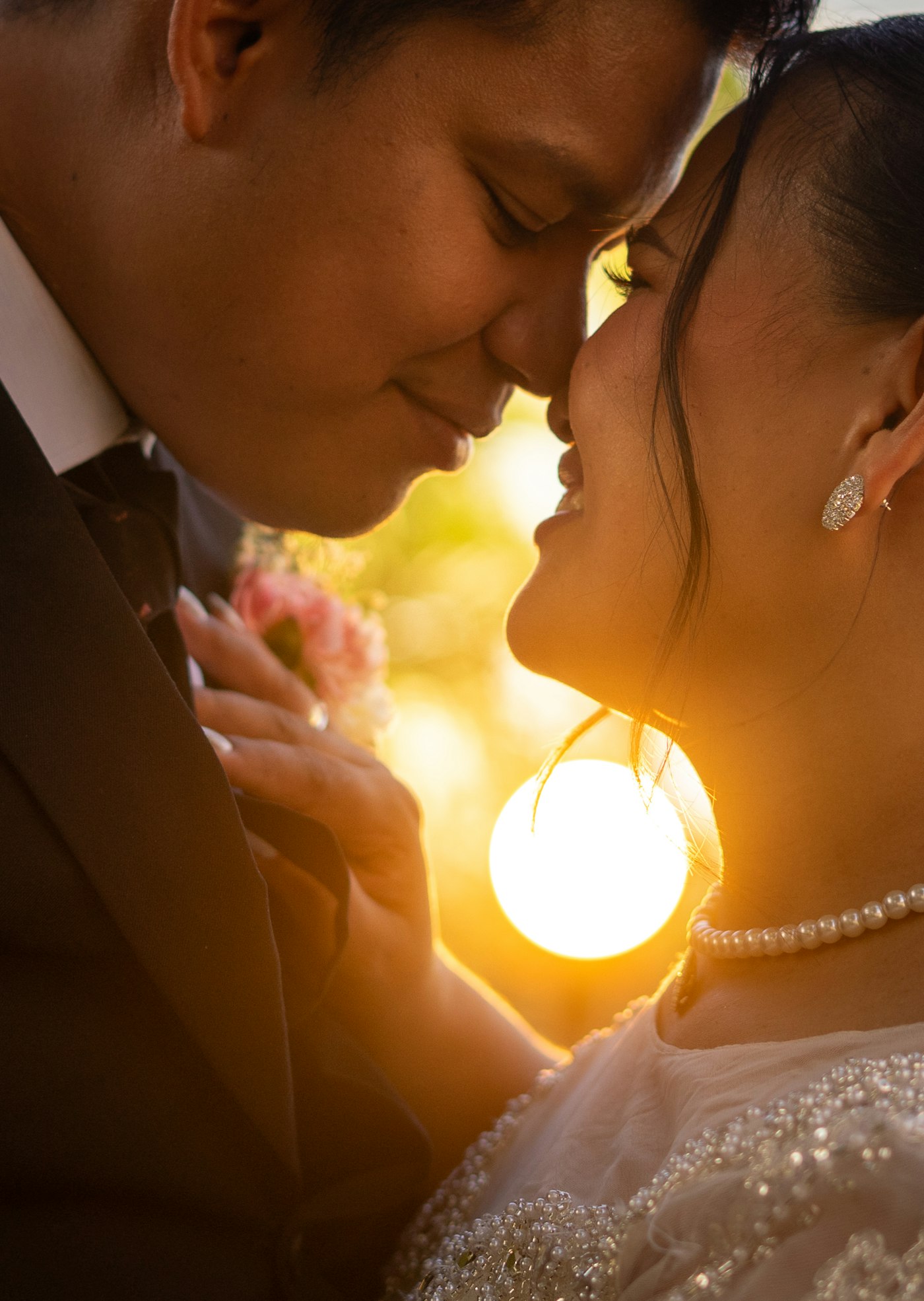 Couple forehead to forehead at sunset, the sun flaring between them