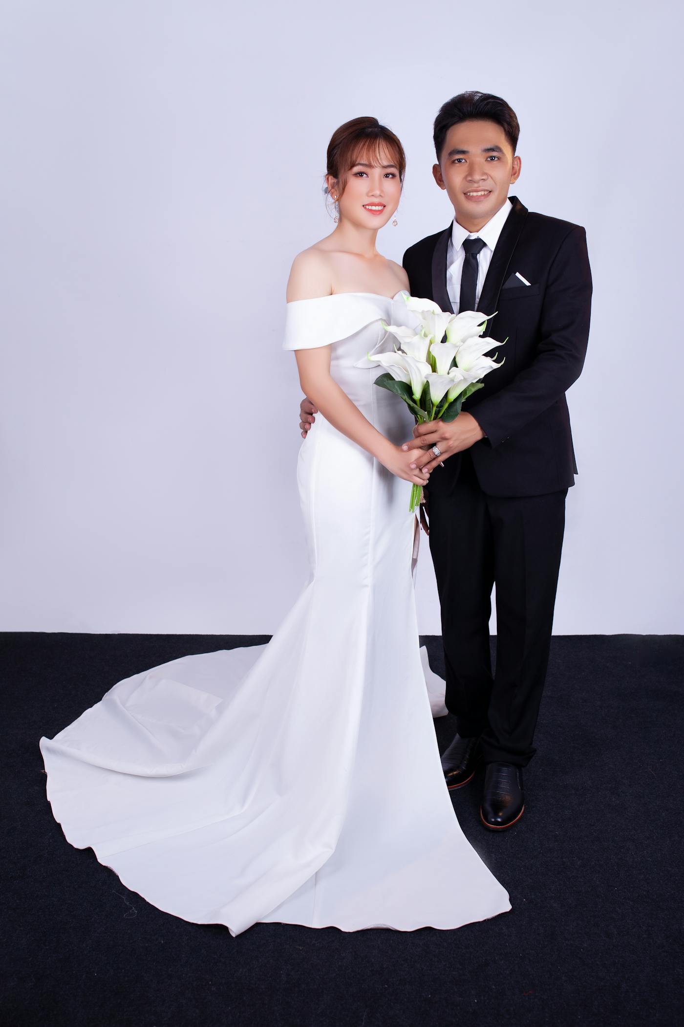 Bride and groom side by side in the studio, holding white calla lilies